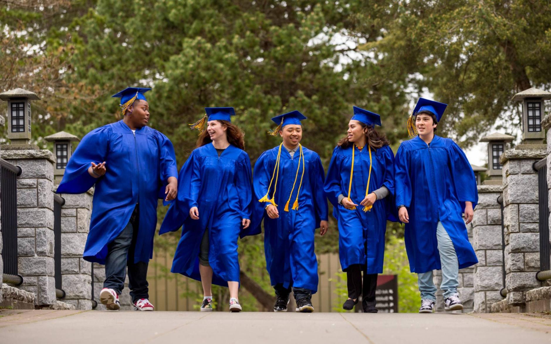 Students in graduation regalia walk across the Japanese bridge on campus